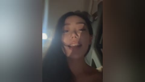 Video of an Asian woman with long black hair, smiling, standing in a dimly lit room with a mirror reflection.