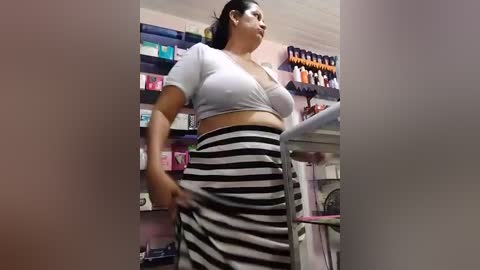 A video of a plus-sized woman with medium-dark skin and dark hair, wearing a white crop top and black-and-white striped skirt, in a pharmacy aisle.