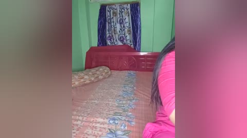 A video showing a flooded bedroom with a green wall, a red bed with floral bedding, a blue curtain, and a person with long black hair in a bright pink shirt partially visible.