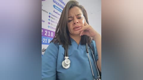 A video of a Hispanic woman with shoulder-length brown hair, wearing a blue hospital gown, and holding a stethoscope, looking distressed and touching her chin in a clinical setting.