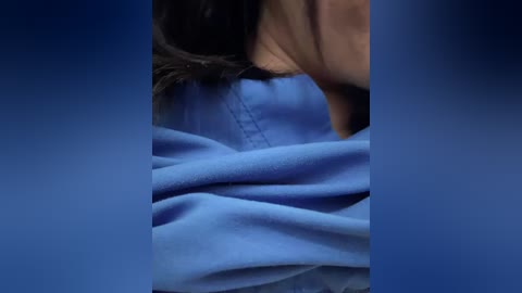 Video of a close-up of a person with dark hair, wearing a blue shirt, leaning forward. The background is a gradient blue, emphasizing the shirt's soft texture.