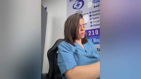 Video of a pregnant woman in blue scrubs, sitting on a black office chair, with a blue and white office wall featuring a health insurance company logo in the background.