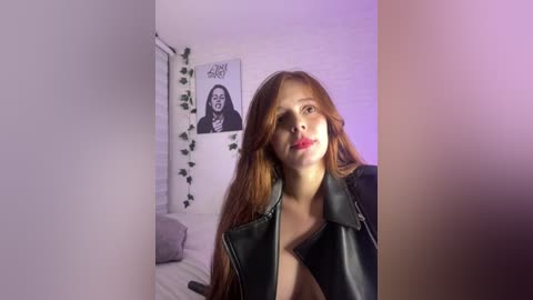 Video of a young woman with long, wavy red hair, wearing a black leather jacket, in a dimly lit bedroom with purple lighting, a poster of Jimi Hendrix, and green vines on the wall.