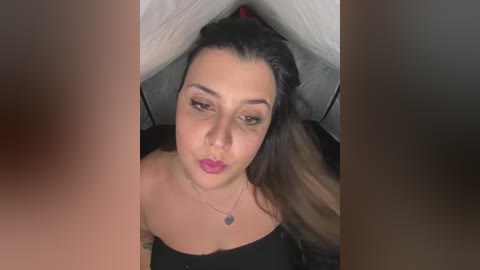 Video of a woman with medium skin tone, long dark hair, and bold makeup, including dark eyeliner and pink lipstick, lying in a tent.