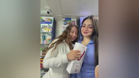 Video of two women, one in white jacket, the other in blue scrubs, shopping for groceries. Background shows shelves stocked with various products.