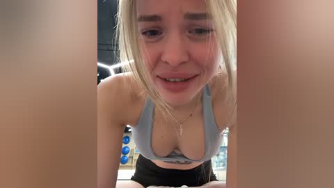 Video of a blonde woman with light skin and a fit physique, wearing a light blue sports bra, looking up with a playful expression.