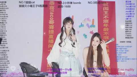 Video of two East Asian women singing into microphones, wearing traditional Chinese clothing. Background features Chinese text and colorful banners.