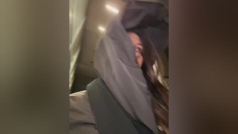 A blurry video of a person with medium skin tone, wearing a dark grey hoodie, slumped over in a car's backseat. The car interior is dimly lit, creating a somber atmosphere.