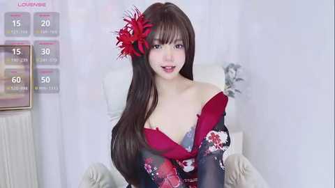 Video of an Asian woman with long brown hair, wearing a red floral kimono, sitting on a white chair, with a red flower in her hair.