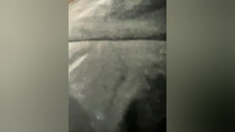 A close-up video of a pale, textured surface, possibly stone or concrete, with a slight sheen. The image is grainy, with indistinct shadows and highlights, creating a somewhat blurred effect.