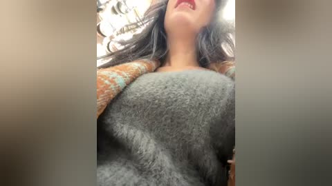 Video of a woman with long dark hair, wearing a gray, fluffy sweater and red lipstick, lying on a soft, beige surface.
