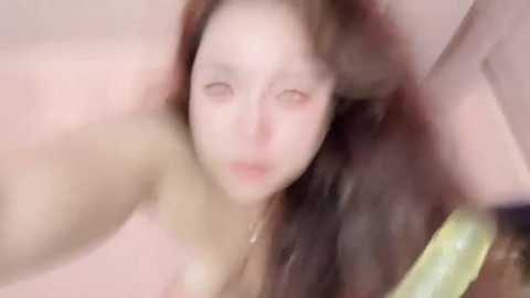 A blurred, soft-focus video of a young woman with light skin and long, wavy brown hair, partially submerged in a bathtub, holding a cucumber. The background is out of focus.