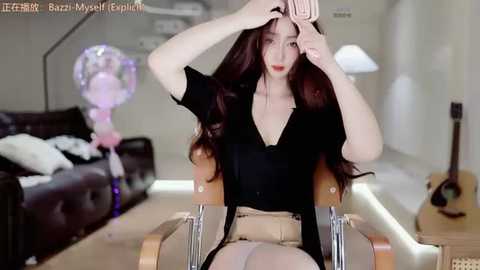 Video of a young woman with long brown hair, fair skin, and a slender figure, sitting on a modern chair in a living room, adjusting her hair, wearing a black blouse and beige skirt, with a guitar and balloons in the background.