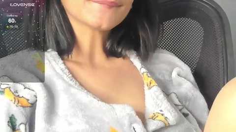 Video of a woman with medium skin tone, wearing a grey pajama top with yellow cartoon characters, sitting in a car.