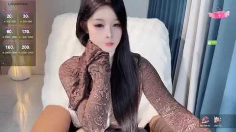 Video of an Asian woman with long black hair, fair skin, and a slender physique, wearing a brown knit sweater, leaning on a white cushion, in a modern room with grey curtains and a lamp.