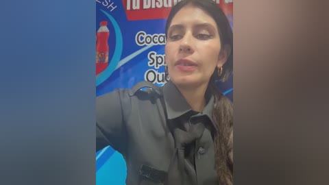 Video of a young woman with long dark hair, wearing a dark shirt and sunglasses, posing against a blue and red backdrop with text.