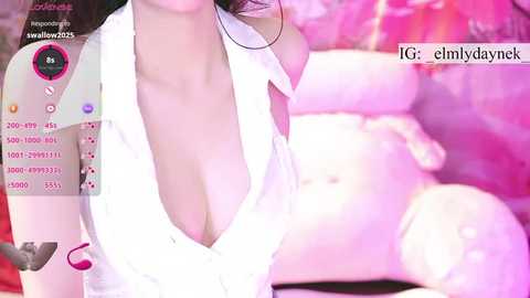 Video of a woman in a low-cut white blouse, lying on a pink bed, with a blurred background, featuring a live stream overlay with social media icons and text.