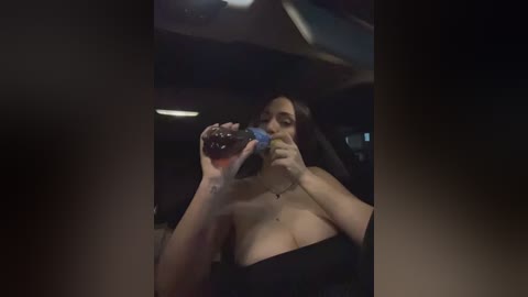 A dimly lit video of a woman with long black hair, wearing a strapless black dress, drinking from a glass at a nightclub.