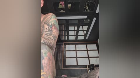 A video of a muscular man with a large, colorful tattoo sleeve on his right arm, standing in a traditional Japanese room with shoji screens and tatami mats.