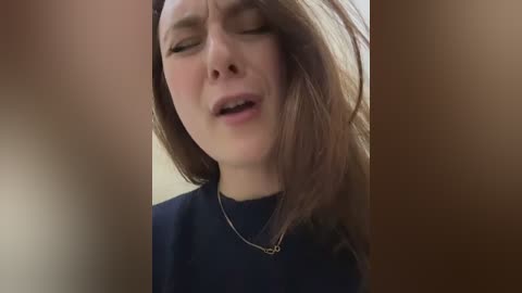 A close-up video of a young woman with light skin and straight, brown hair, wearing a dark top and a silver necklace, eyes closed in what appears to be an intimate moment.