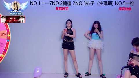 Video of two young women, one in black, the other in white, performing against a white backdrop.