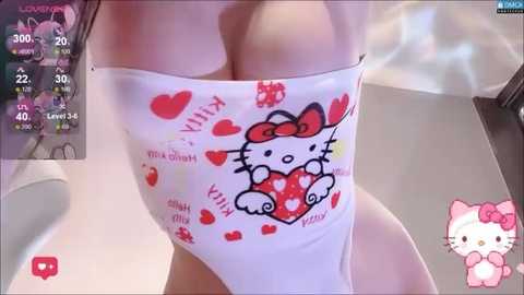 Video of a woman wearing a white top with a Hello Kitty design, standing indoors. The background shows a virtual chat window and a Hello Kitty plush toy.