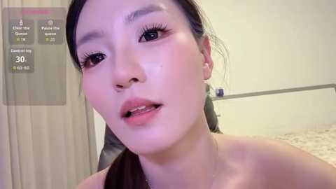 A video of an Asian woman with light skin, long dark hair, and minimal makeup, wearing a strapless top, taken indoors with a virtual temperature gauge overlay.