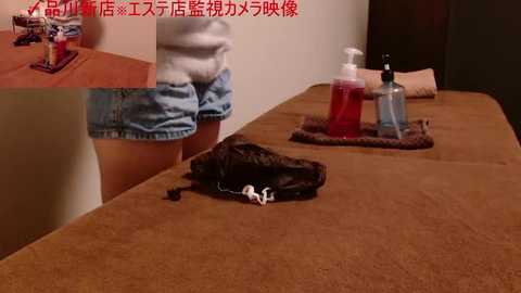 A video of a woman wearing denim shorts and a sweater sitting on a brown massage table. A small black dog rests on the table.