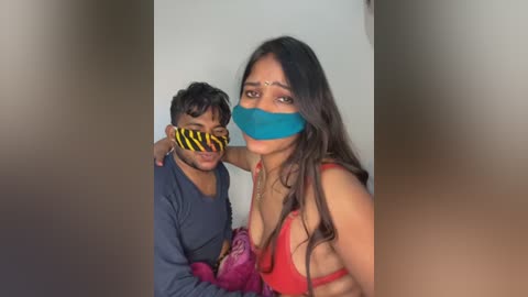 Video of a man with short hair in a blue shirt and a woman with long hair in a red bra, both gagged with blue tape, in a dimly lit room.