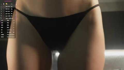A close-up video of a woman's lower torso in black thong underwear, showcasing fair skin and a slim physique. The background is blurred, with a digital interface displaying health and fitness data.