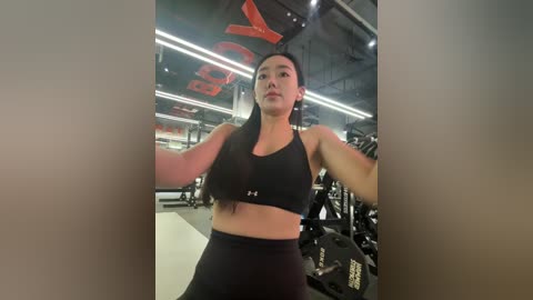 A video of a woman lifting weights in a modern gym, wearing a black sports bra and high-waisted leggings, surrounded by gym equipment and red lighting.