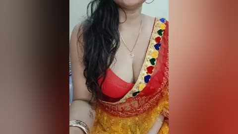 Video of a woman in a red sari with gold embroidery and colorful hearts, wearing a red bra underneath, revealing cleavage, with long, wavy black hair and a silver necklace.
