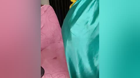 Video of two fabric swatches: a pink floral pattern and a teal solid. The background shows a black curtain with a yellow decorative element.