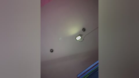 Video of a modern indoor ceiling with three recessed lights, one emitting a bright, white light, and another with a dim, yellowish glow. The ceiling is white, and a window with colored curtains is partially visible in the background.