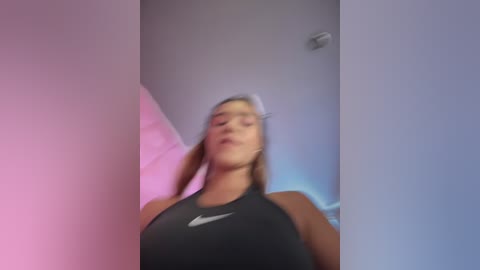 Video of a woman with light skin and long blonde hair, wearing a black Nike sports bra, standing in a dimly lit room with purple and pink lights.
