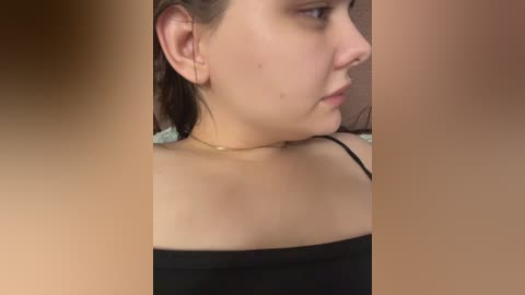 Video of a young Caucasian woman with fair skin, a nose ring, and brown hair pulled back, wearing a black off-shoulder top. Background is blurred, focusing on her profile.