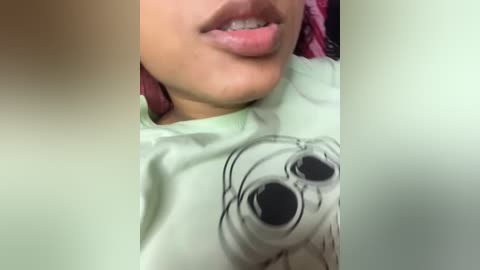 Video of a light-skinned person with pink hair, wearing a green shirt with a cartoon character, partially cropped.