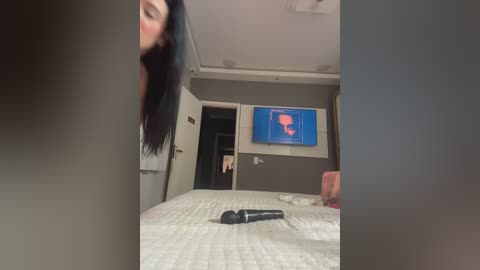 A video of a woman in a bedroom with a television showing a blue screen. She is smiling, holding a black object.