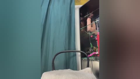 A video of a medical examination room with teal curtains, a black metal chair, and a glass cabinet displaying medical equipment and a pink flower arrangement.