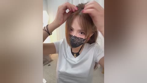 Video of an Asian woman with fair skin, wearing a black lace mask, white T-shirt, and long brown hair. She's in a bathroom, adjusting her hair, with blurred, partially visible figures in the background.
