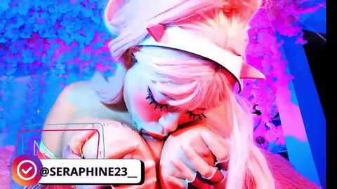 A vibrant, digital video of a blonde woman in a white hat, with pink and blue lighting, holding a phone, set against a textured background.