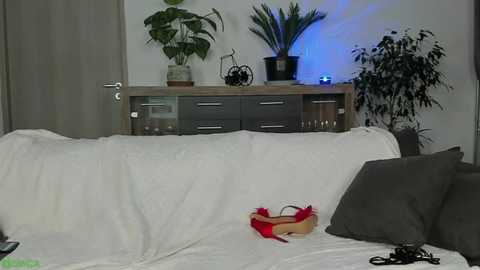Video of a modern living room with a white couch, dark wooden TV stand, potted plants, and electronic cables.