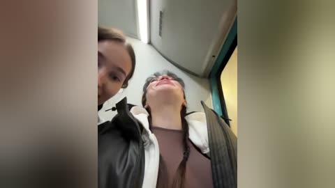 Video of a young woman with fair skin and brown hair, wearing a black jacket and brown top, leaning back, eyes closed, inside a dimly lit, modern bus.