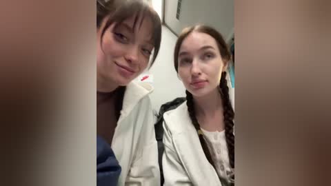 A video of two young women, one with straight brown hair, the other with braided brown hair, wearing white lab coats, in a clinical setting.
