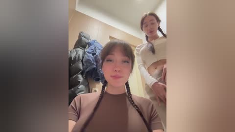 Video of two Asian women in a closet, one wearing a brown shirt and the other a beige sweater, with jackets and coats hanging in the background.