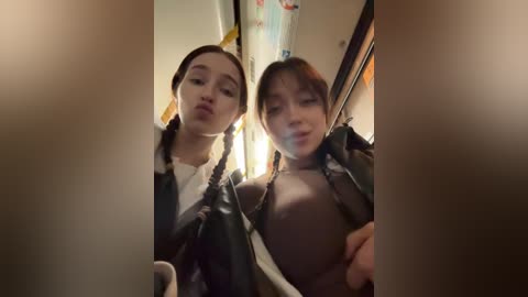 Video of two Asian women with braided hair, one topless with small breasts, the other partially clothed, posing intimately indoors, with blurred background.