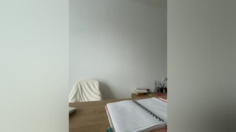 Video of a minimalist office space with a beige wall, a white chair, wooden desk, open notebook, and scattered office supplies.