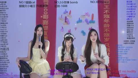 Video of three young Asian women in colorful, sleeveless dresses singing into microphones against a colorful, light-up background. Text in Chinese is visible.