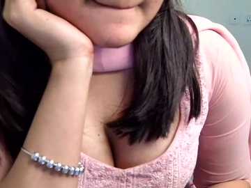 Video of a woman with medium skin tone, wearing a light pink lace top and a silver bracelet, resting her chin on her hand, smiling, with long black hair partially visible.