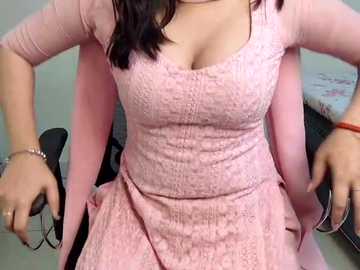 Video of a woman in a pink lace dress with a plunging neckline, seated on a black chair, wearing a bracelet on her right wrist.